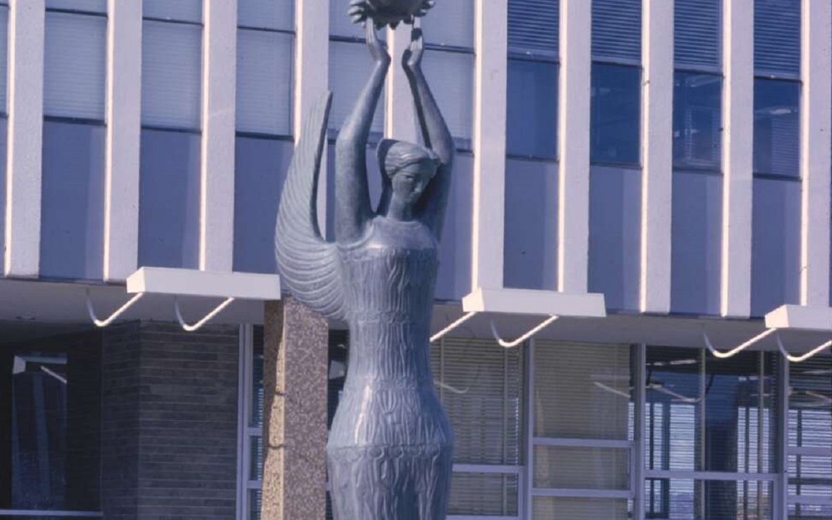 A statue of a female form holding a sunburst above her head.