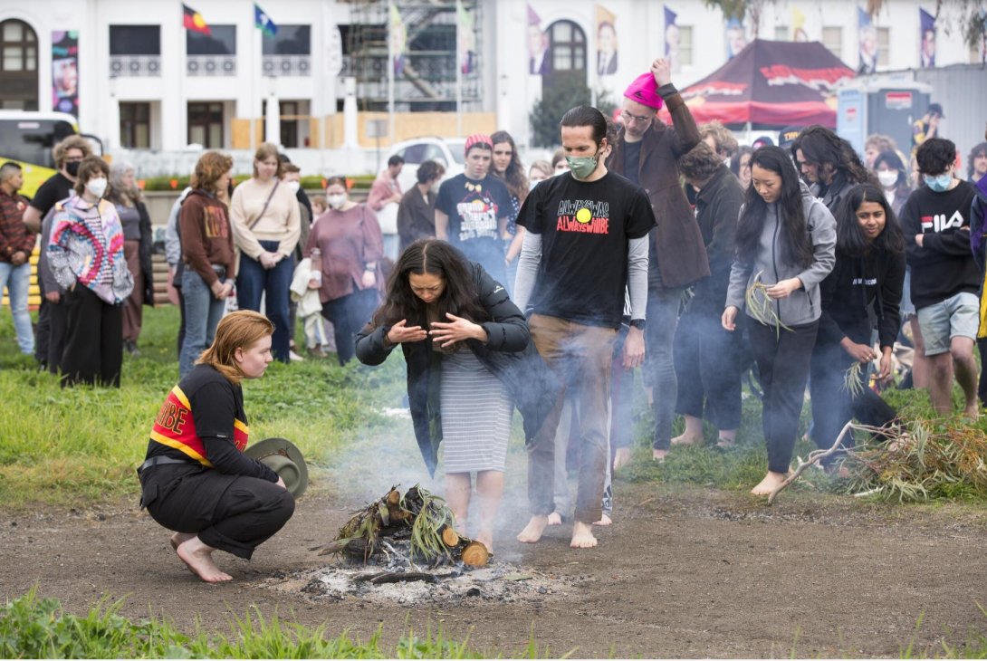 A line of people queuing to take part in a smoking ceremony. Old Parliament House is in the background.